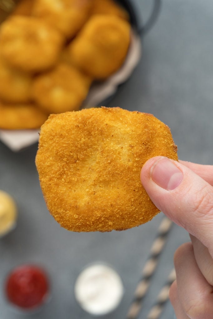 a hand holding up a homemade breaded chicken nugget