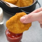a hand dunking a homemade chicken nugget in a little glass of ketchup