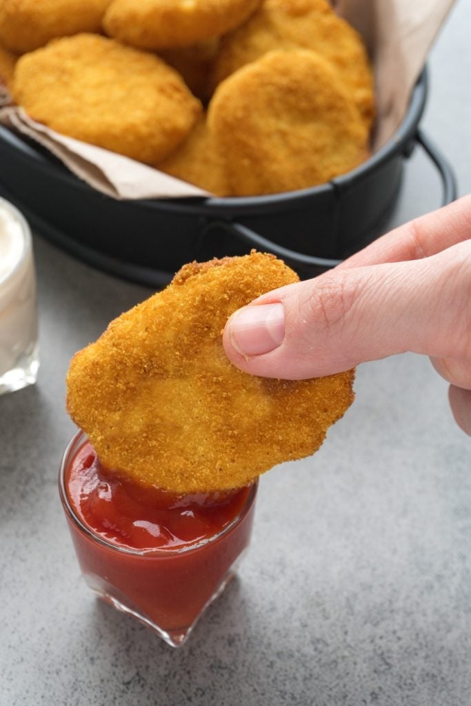 a hand dunking a homemade chicken nugget in a little glass of ketchup