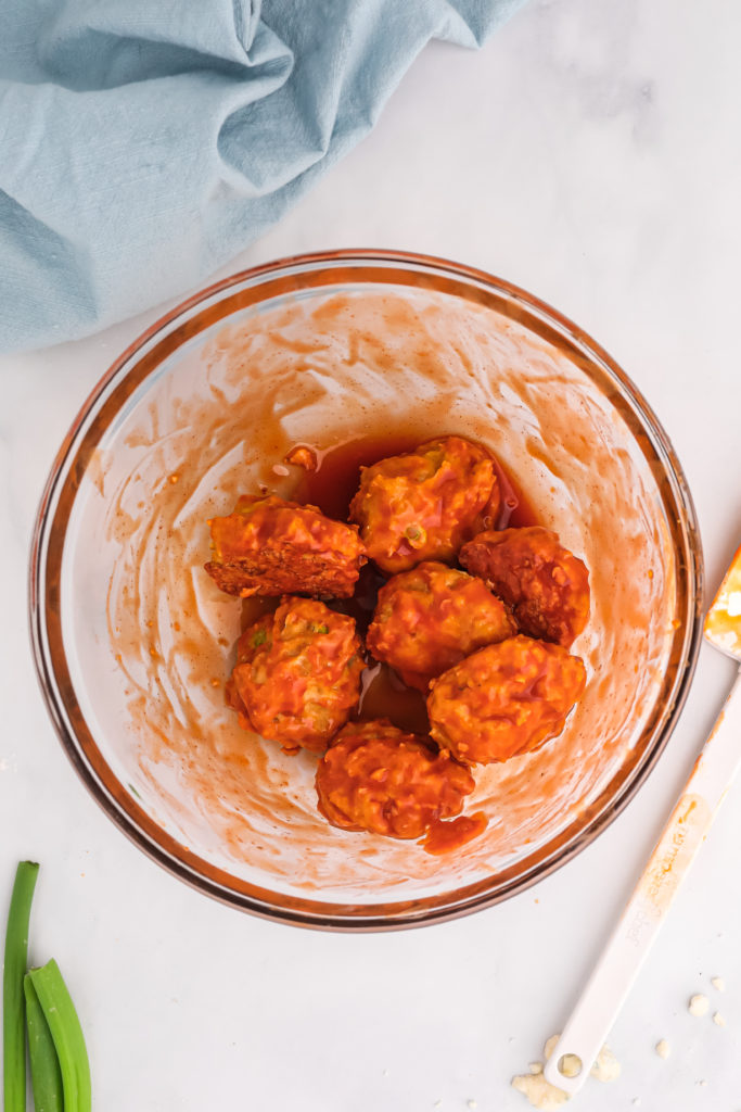 buffalo chicken meatballs in a glass bowl tossed with hot sauce