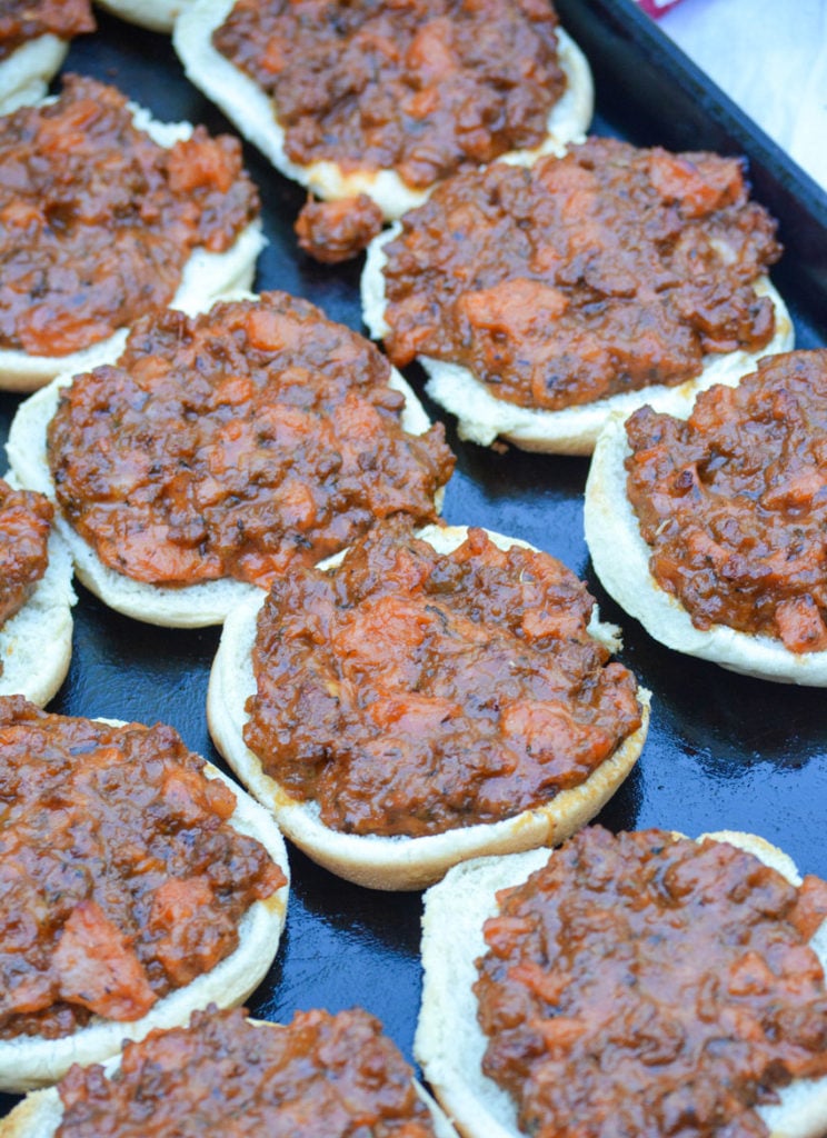 cafeteria style pizza burgers arranged on a large, dark metal baking pan