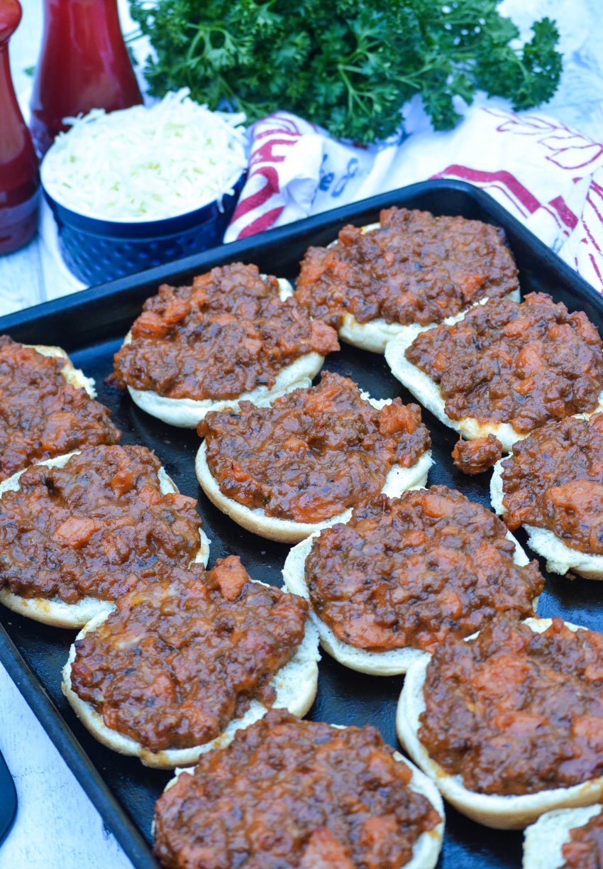 cafeteria style pizza burgers arranged on a large, dark metal baking pan