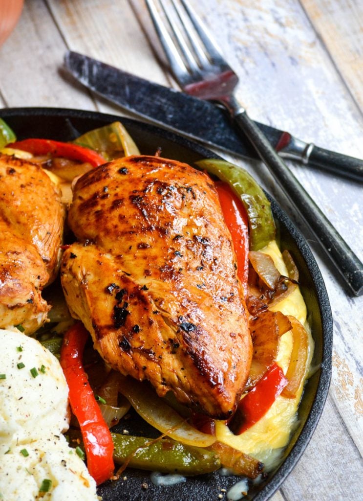 copycat TGIFriday's sizzlin chicken & cheese on a flat cast iron skillet next to a pair of silverware