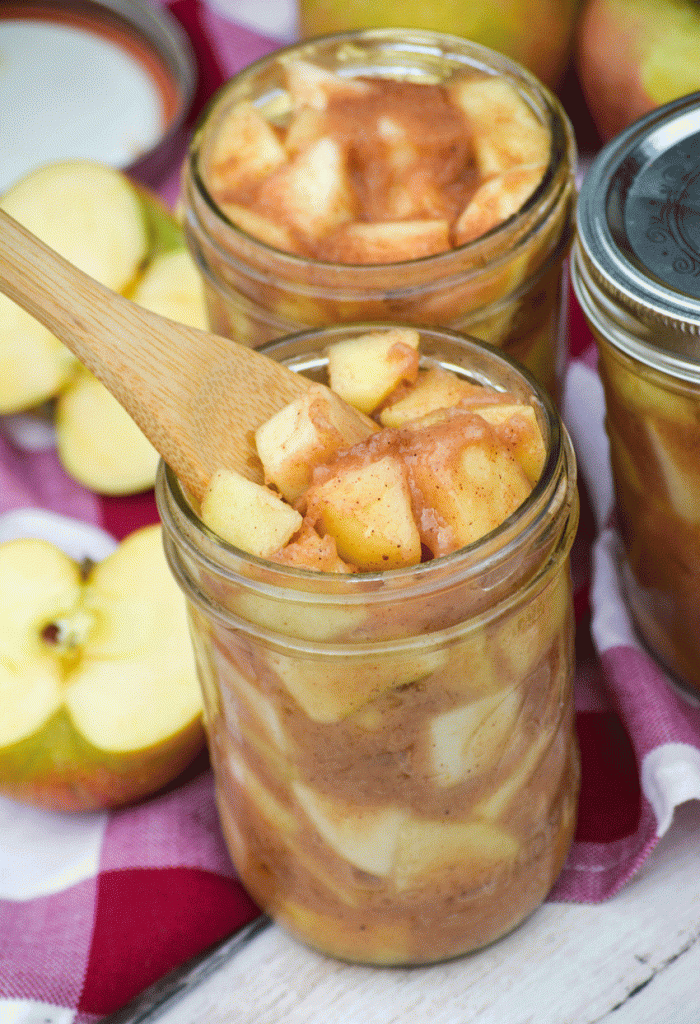 a wooden spoon stuck in a glass jar filled with crockpot apple pie filling