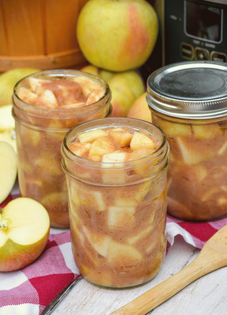 crockpot apple pie filling in glass mason jars in front of a silver slow cooker