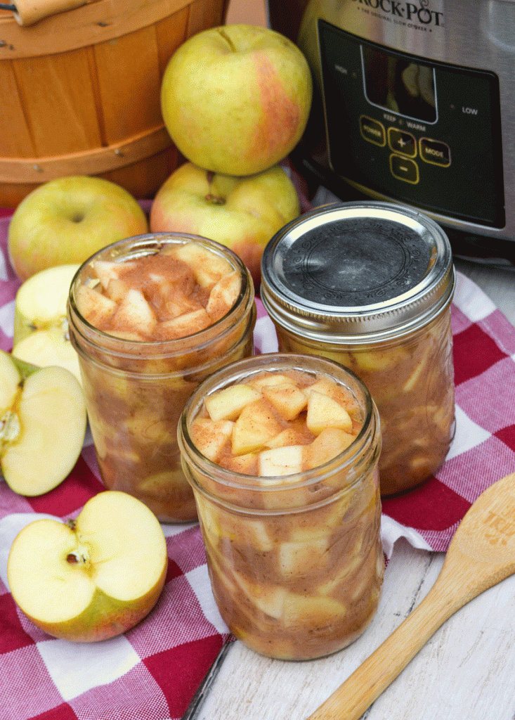 crockpot apple pie filling in glass mason jars in front of a silver slow cooker
