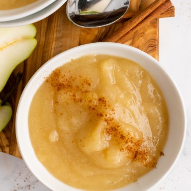 Instant pot pear sauce served in a white bowl & sprinkled with ground cinnamon