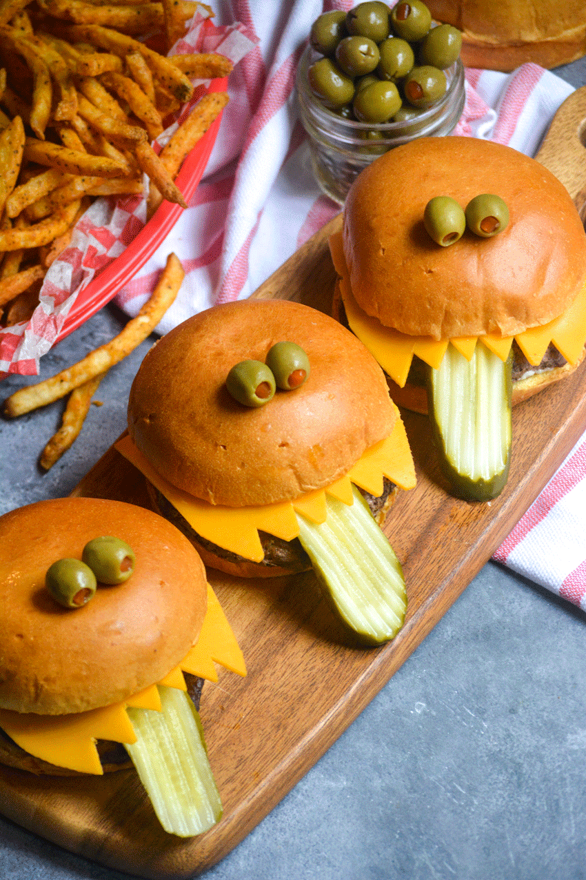 three monster burgers lined up on a wooden cutting board