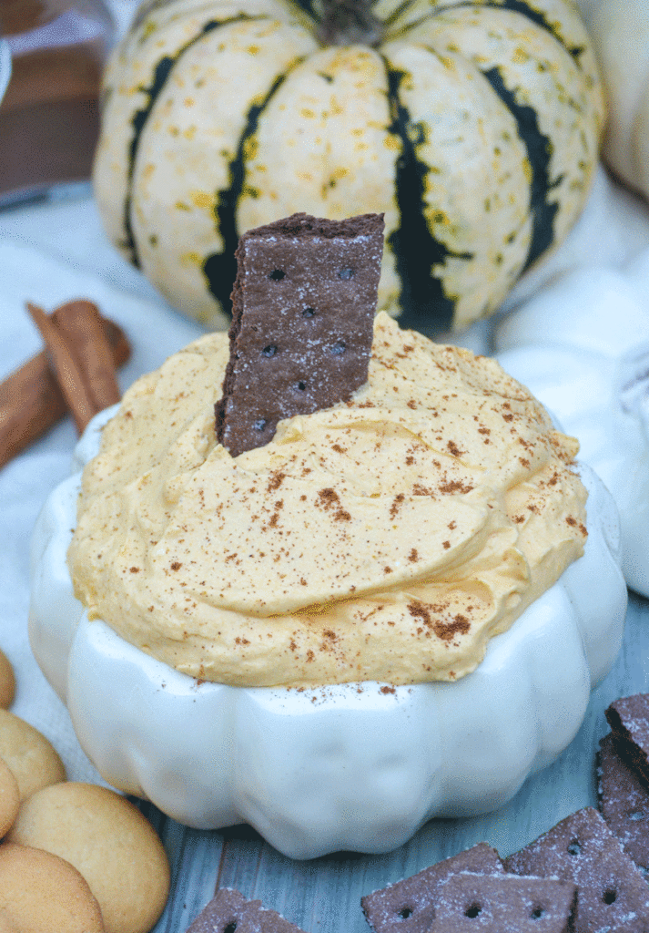 pumpkin cheesecake dip in a white ceramic pumpkin shaped bowl with a graham cracker stuck in the middle of the dip