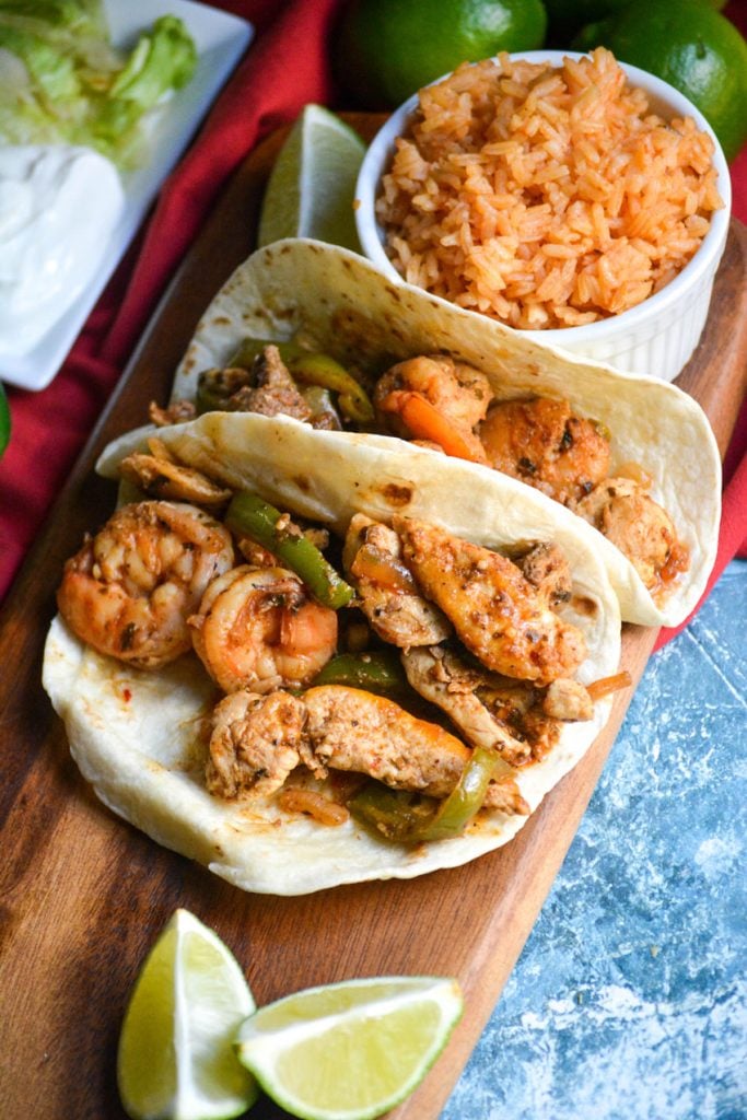 Texas fajitas arranged on a narrow wooden cutting board with a small bowl of spanish rice