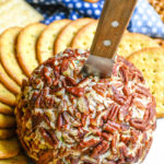 pecan coated basic cheeseball with a spreader sticking out the top surrounded by large crackers