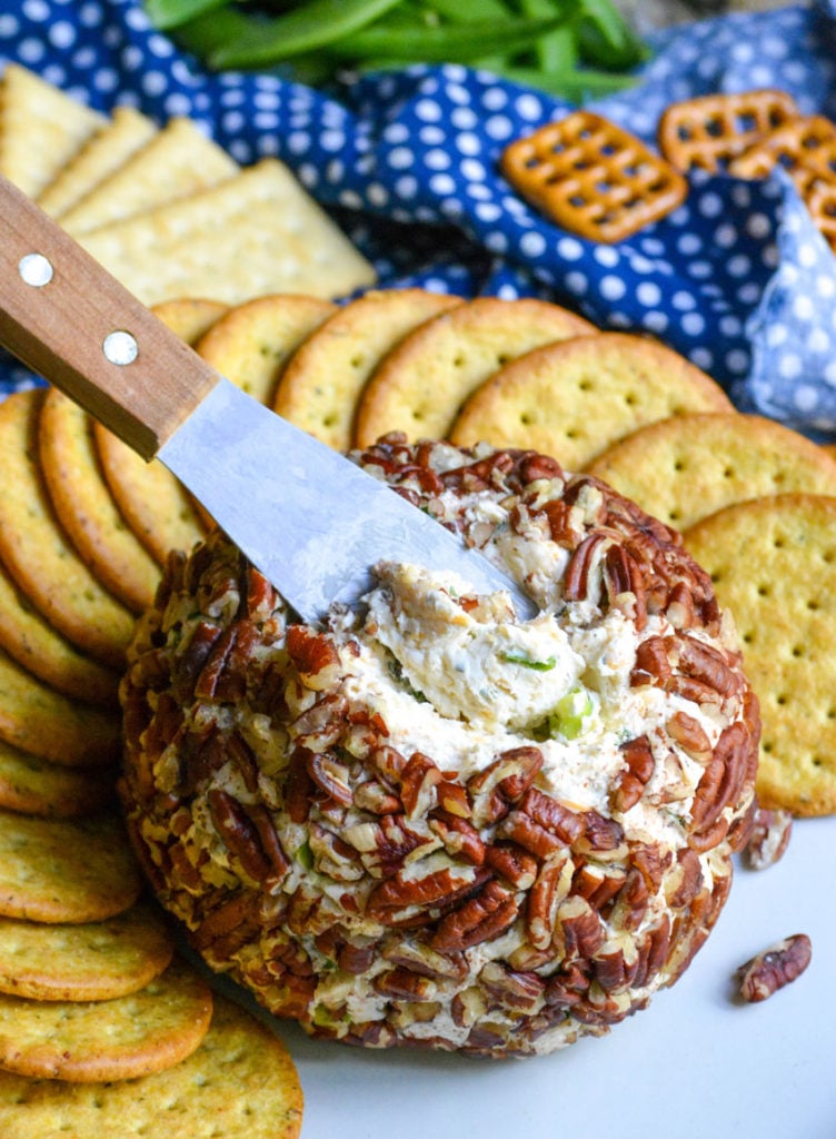 a wooden spreader digging into the cream cheese center of a nut crusted cheeseball