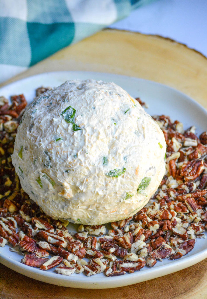 seasoned cream cheeseball on a bed of crushed pecans in the center of a white plate