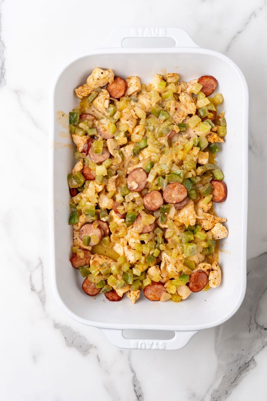 LASAGNA NOODLES TOPPED WITH CAJUN SEASONED MEAT AND VEGGIES IN A WHITE BAKING DISH