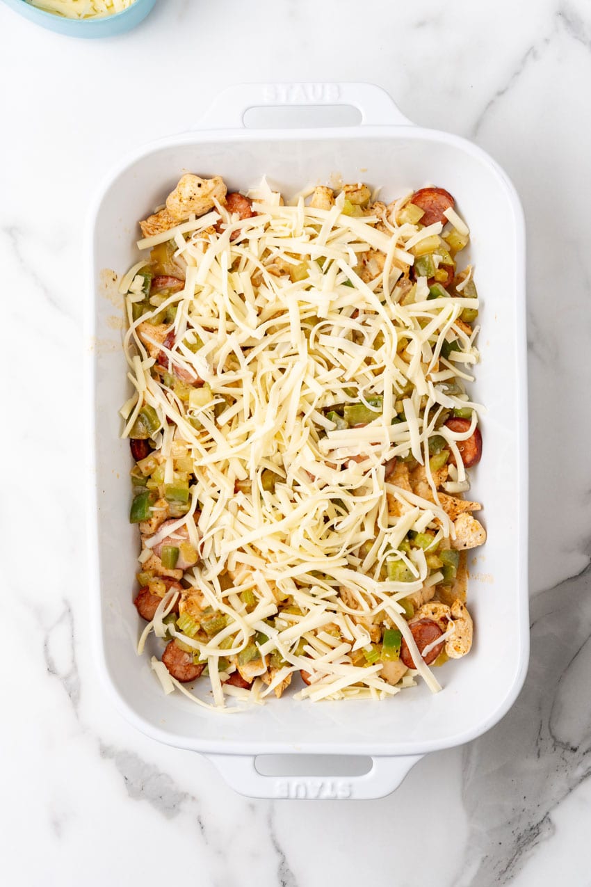 LASAGNA NOODLES TOPPED WITH CAJUN SEASONED MEAT AND VEGGIES IN A WHITE BAKING DISH