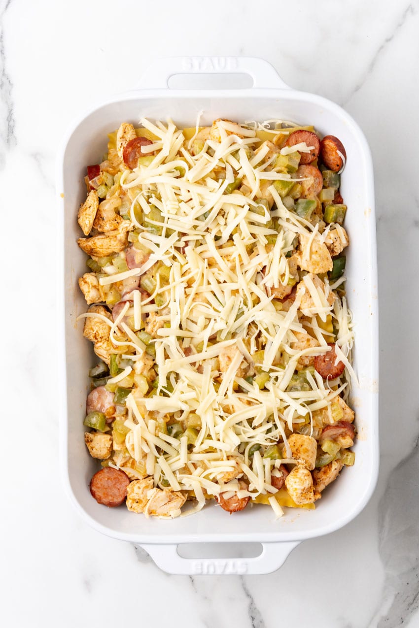 layers of LASAGNA NOODLES TOPPED WITH CAJUN SEASONED MEAT AND VEGGIES and alfredo sauce IN A WHITE BAKING DISH