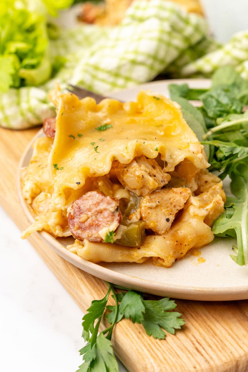 a slice of cajun lasagna on a white plate with fresh greens on the side