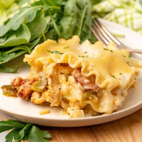 a slice of cajun lasagna on a white plate with fresh greens on the side