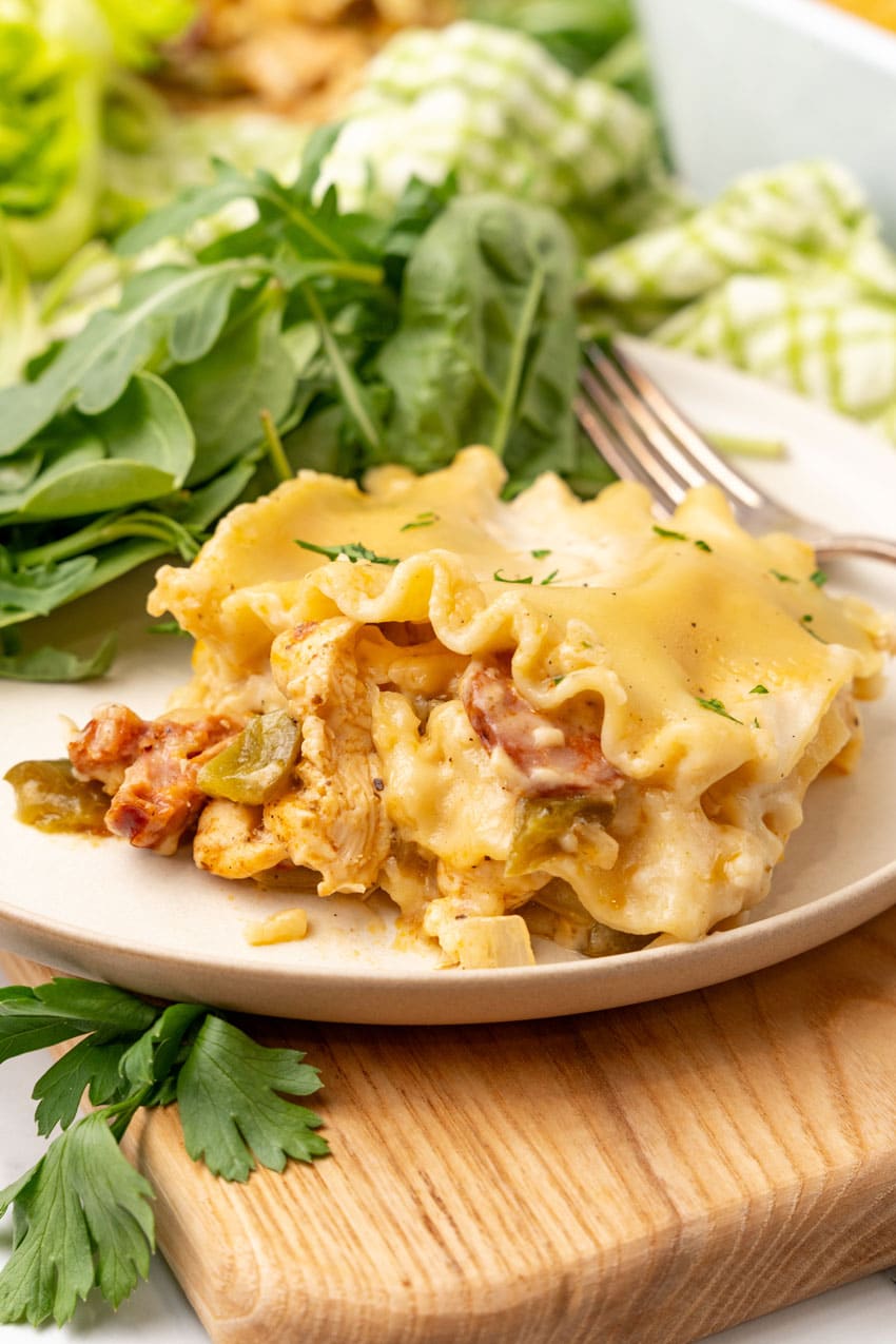 a slice of cajun lasagna on a white plate with fresh greens on the side