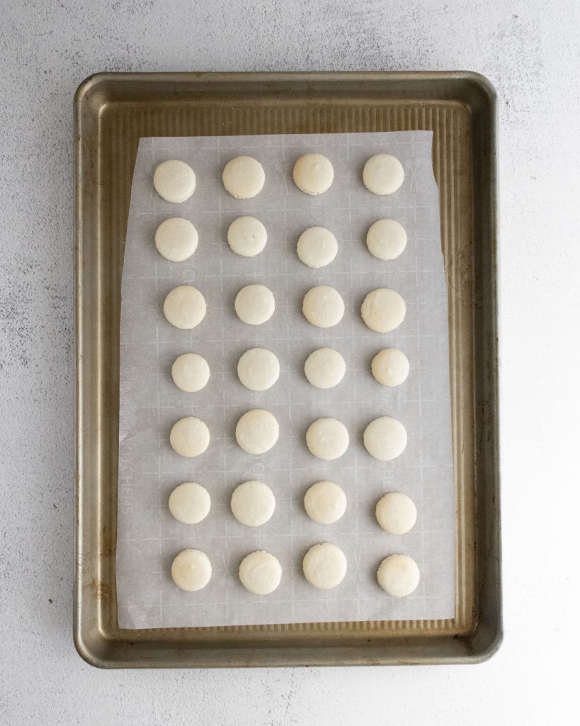 white macaron shells on a parchment lined baking sheet