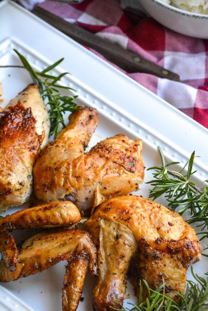 air fryer rotisserie chicken cut up into pieces on a white platter with sprigs of fresh rosemary