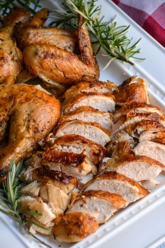 air fryer rotisserie chicken cut up into pieces on a white platter with sprigs of fresh rosemary with the two breasts shown sliced