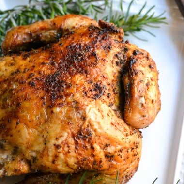 air fryer rotisserie chicken on a white plate with sprigs of fresh rosemary