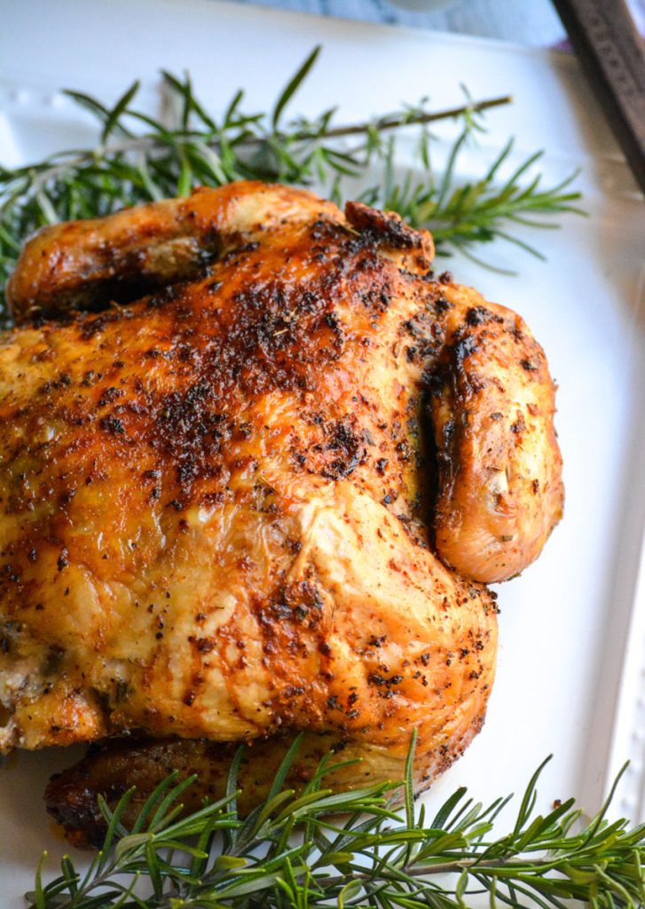 air fryer rotisserie chicken on a white plate with sprigs of fresh rosemary