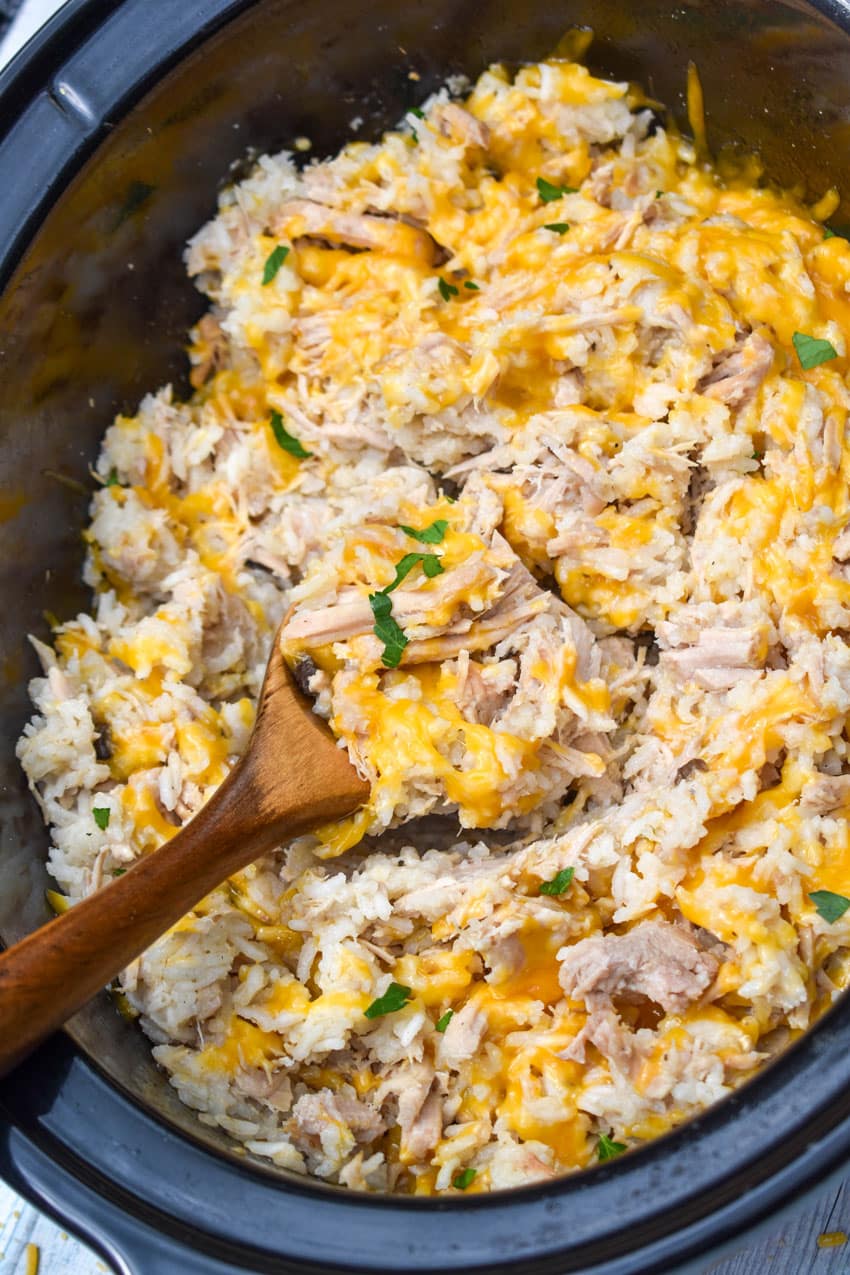 a wooden spoon scooping cheesy pork and rice out of a crockpot