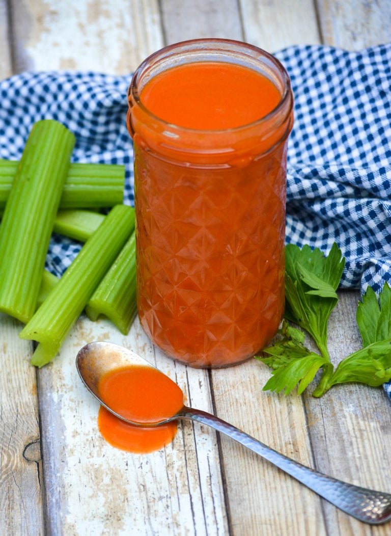 homemade buffalo sauce in a glass mason jar and shown in a silver spoon on the side