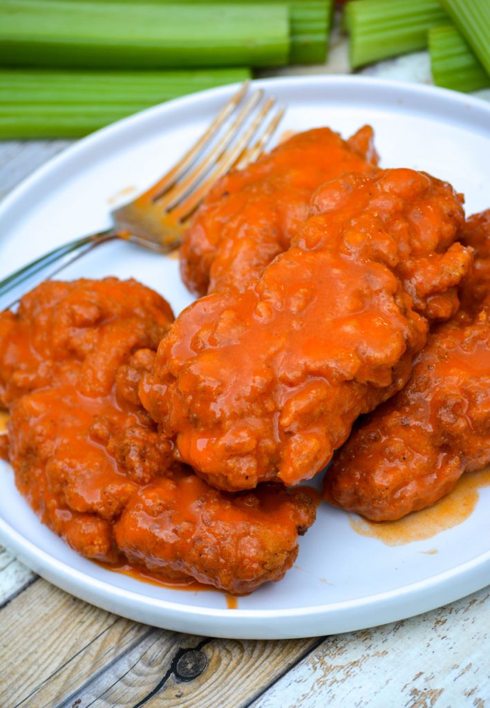 buffalo wing sauce tossed chicken strips on a white plate