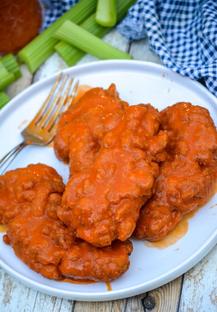 buffalo wing sauced crispy chicken on a white plate with a silver fork to the side