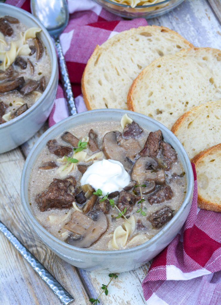 beef stroganoff soup served in two gray bowls with dollops of fresh sour cream with sliced bread on the side