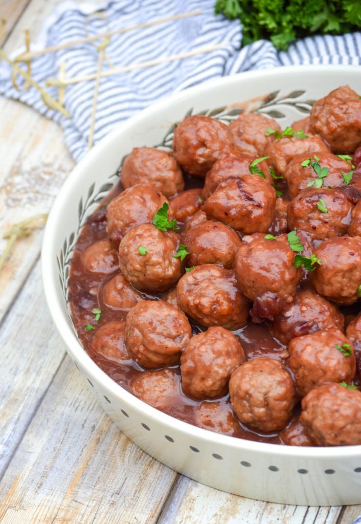 crockpot cranberry orange meatballs in a white serving dish topped with fresh chopped green herbs