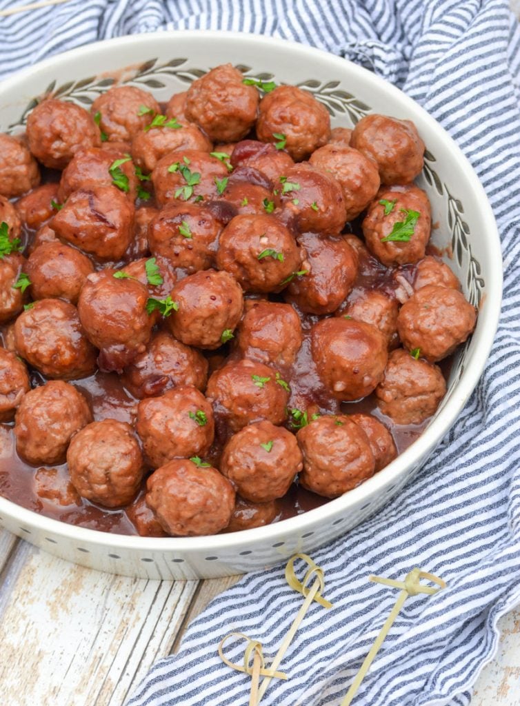 slow cooker cranberry orange meatballs in a white serving dish topped with fresh chopped green herbs