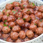 slow cooker cranberry orange meatballs in a white serving dish topped with fresh chopped green herbs