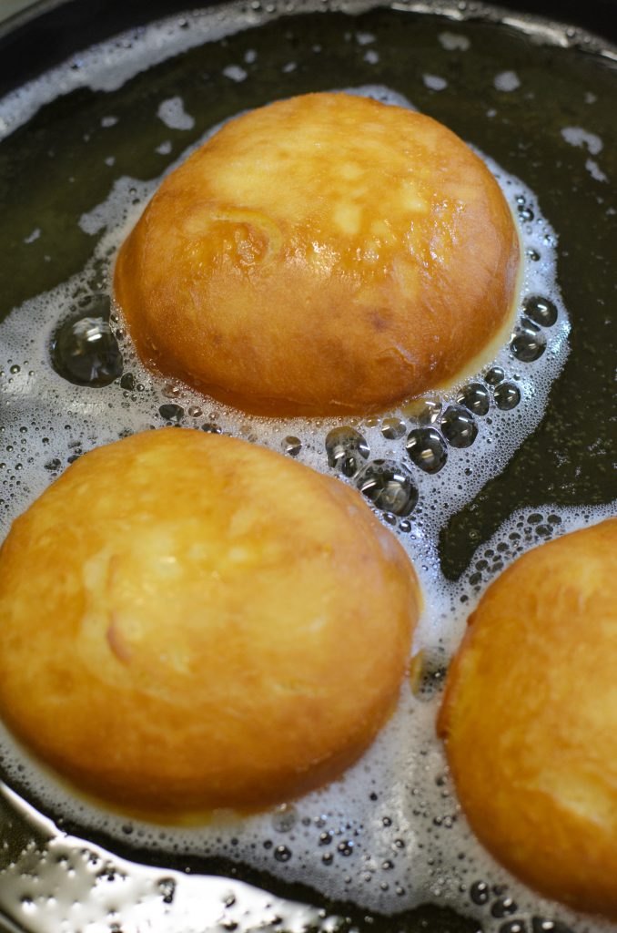golden brown homemade donuts shown surrounded by bubbles frying in hot oil