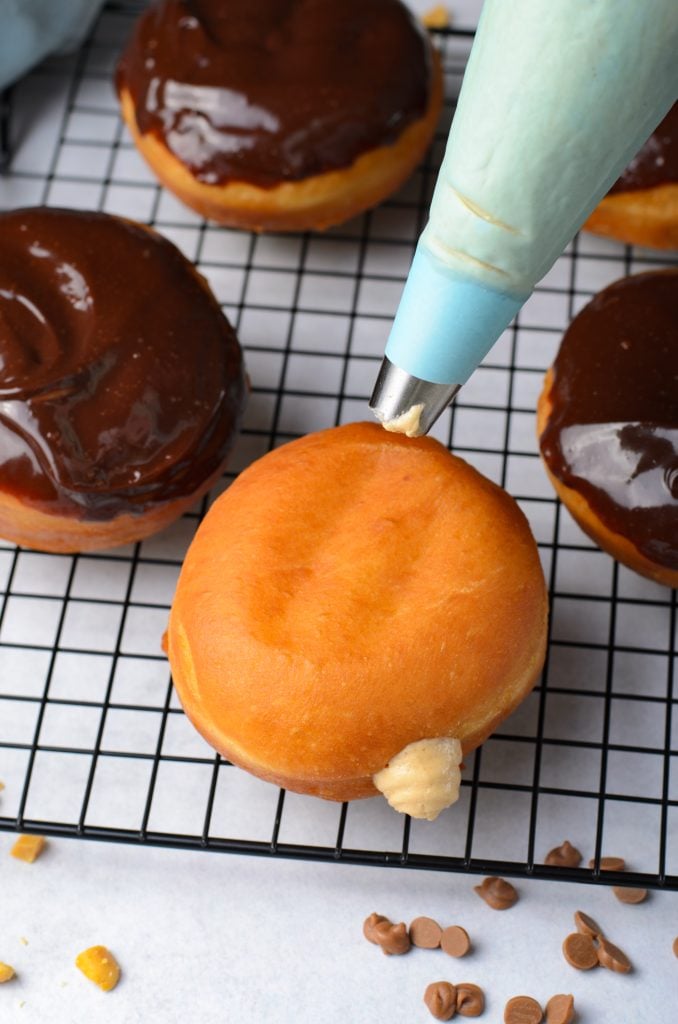 peanut butter mousse shown being piped into the center of a golden brown donut from a piping bag