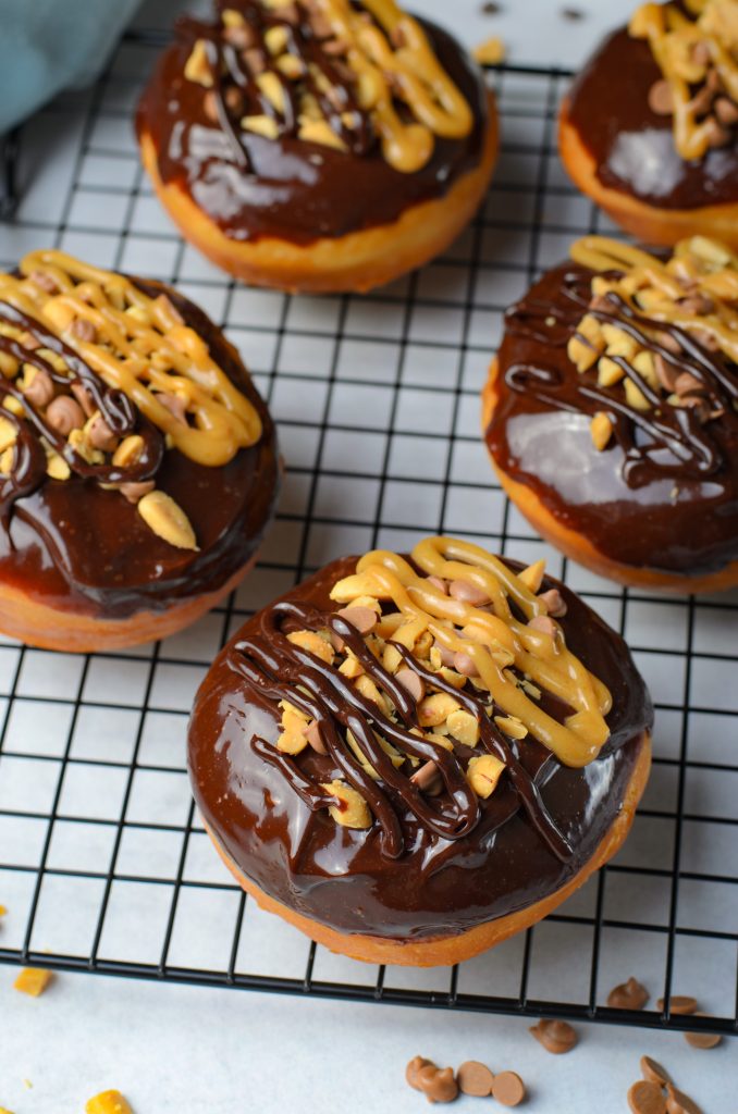 reese's donuts topped with chopped peanuts and chocolate & peanut butter drizzles on a metal cooling wrack