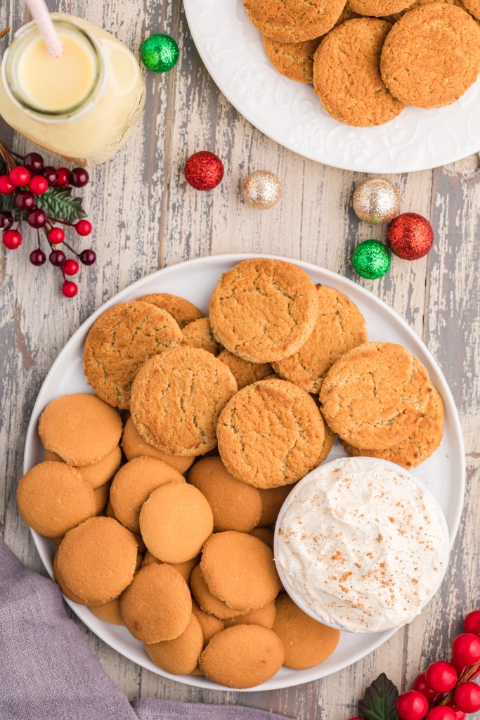 eggnog dip in a white bowl sprinkled with ground cinnamon and surrounded by vanilla wafers and gingersnap cookies