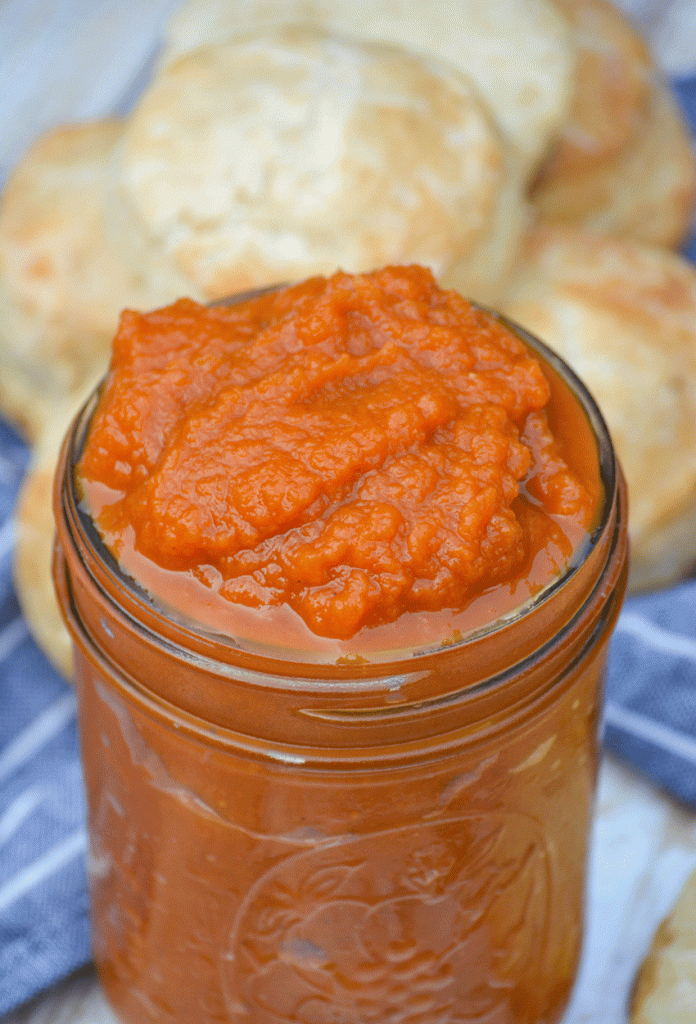 instant pot pumpkin butter piled high in a glass mason jar surrounded by baked biscuits