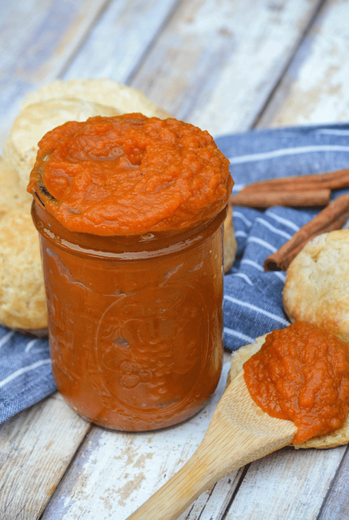 instant pot pumpkin butter piled high in a glass mason jar surrounded by baked biscuits