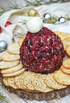 santa hat cranberry cheddar cheeseball on a wooden cutting board surrounded by water crackers