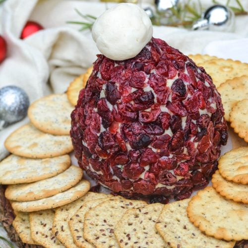 santa hat cranberry cheddar cheeseball on a wooden cutting board surrounded by water crackers