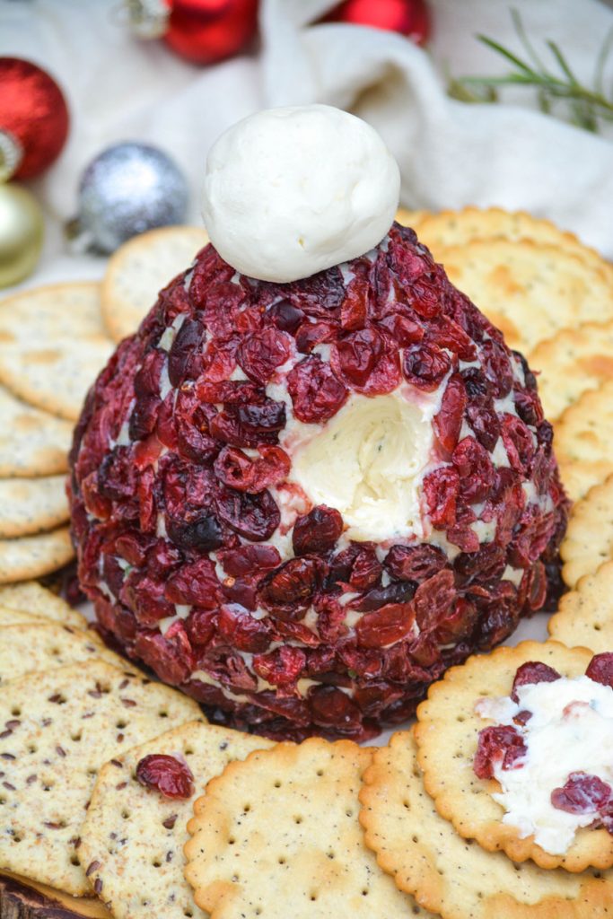 cranberry covered santa hat cheeseball with a hole in the side to reveal the cheese mixture underneath