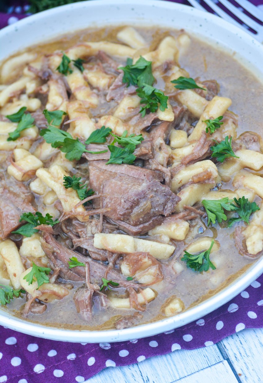 slow cooker beef & noodles topped with fresh green herbs in a shallow white bowl