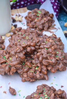 crockpot chocolate peanut clusters topped with sprinkle and arranged on a sheet of white parchment paper