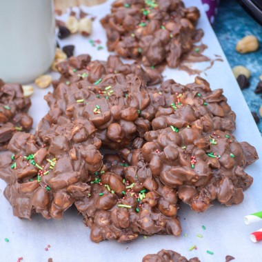 crockpot chocolate peanut clusters topped with sprinkle and arranged on a sheet of white parchment paper