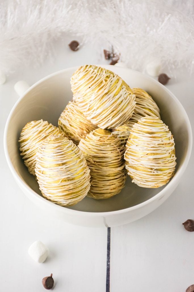 eggnog hot cocoa bombs drizzled with golden chocolate piled high in a white bowl