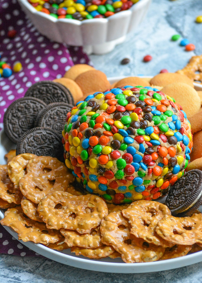 monster cookie cheeseball surrounded by cookies and pretzels on a white plate